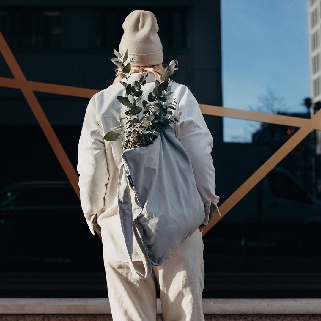 Vrouw draagt grijze Notabag rugzak met planten erin