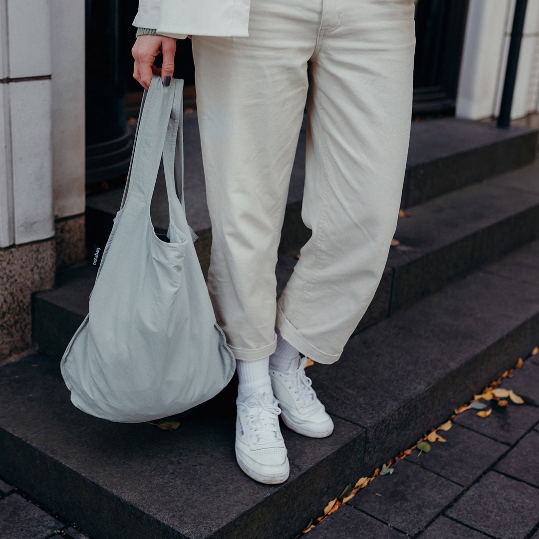 Vrouw met grijze Notabag shopper in de hand op een trap