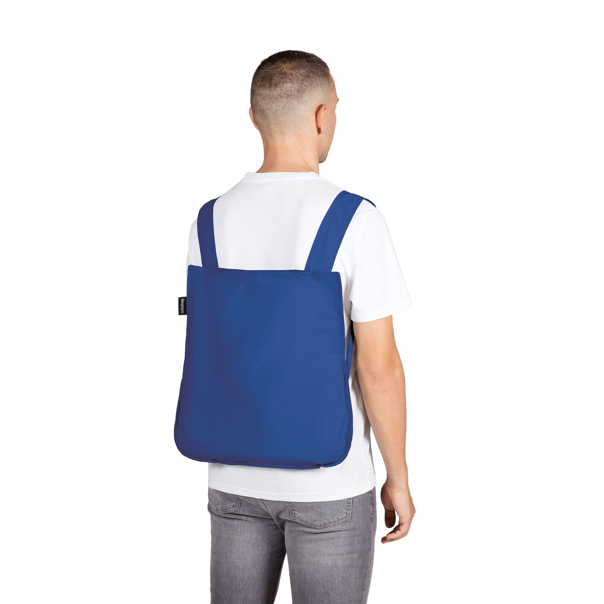 Mann trägt Notabag Royal Blue Rucksack vor weißem Hintergrund