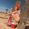 Vrouw zit op het strand tegen een palm met Notabag Red & Purple Stripes shopper