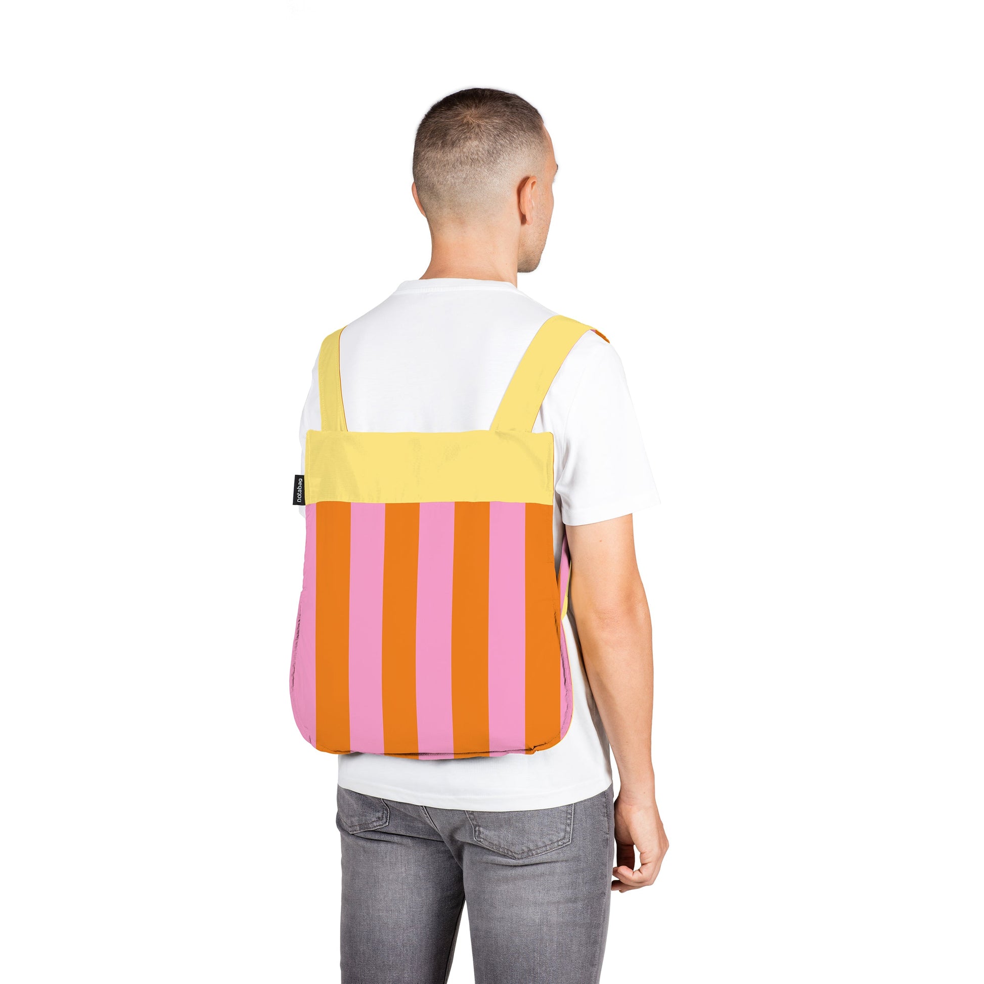 Man wears Notabag Vanilla Stripes backpack against a white background