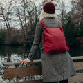 Vrouw met wijnrode Notabag rugzak bij een vijver in het park