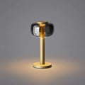 ELLE Decoration Odeon table lamp in matt gold with the light on, against a grey background.