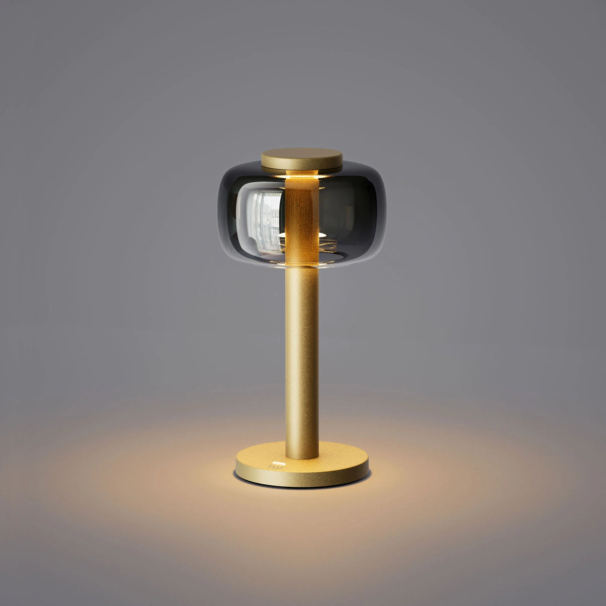 ELLE Decoration Odeon table lamp in matt gold with the light on, against a grey background.