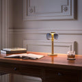 ELLE Decoration Odeon table lamp in matt gold with the light on, on a classic desk.