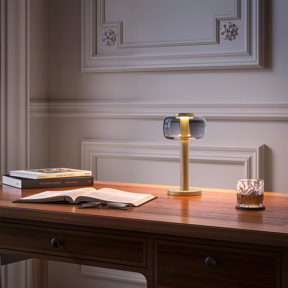 ELLE Decoration Odeon table lamp in matt gold with the light on, on a classic desk.