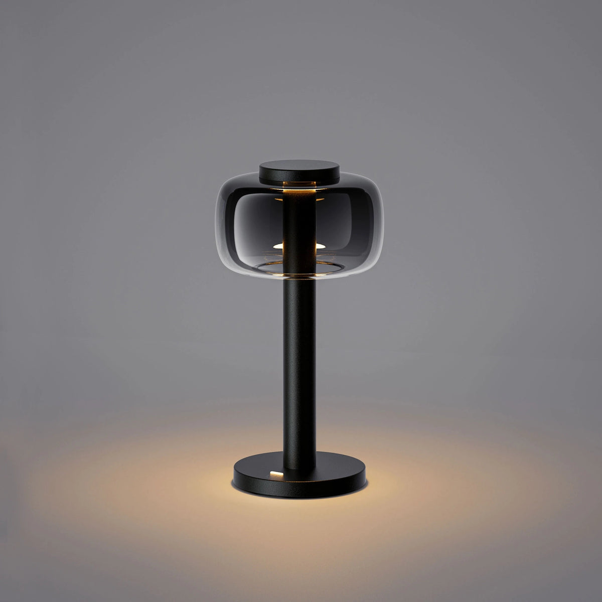 ELLE Decoration Odeon table lamp in matt black with the light on, against a grey background.