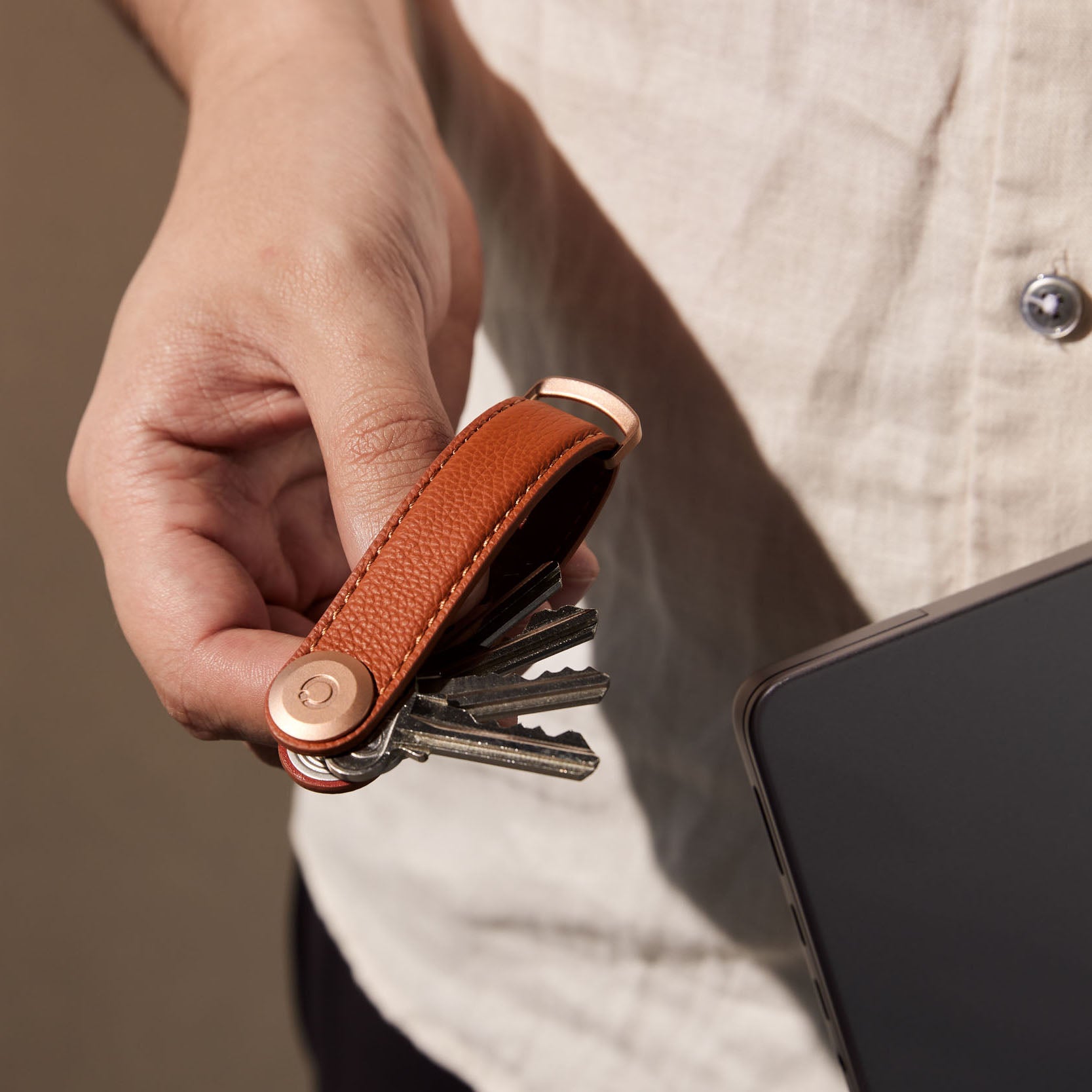 Orbitkey Pebbled Leather Amber│Sleutelhouder│art. KPB2-AMB-101│in hand met uitgevouwen sleutels naast laptop