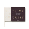 White Be My Guest guest book by Printworks lying flat, half out of its charcoal sleeve
