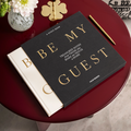 White Be My Guest guest book half out of its charcoal sleeve on a round red table