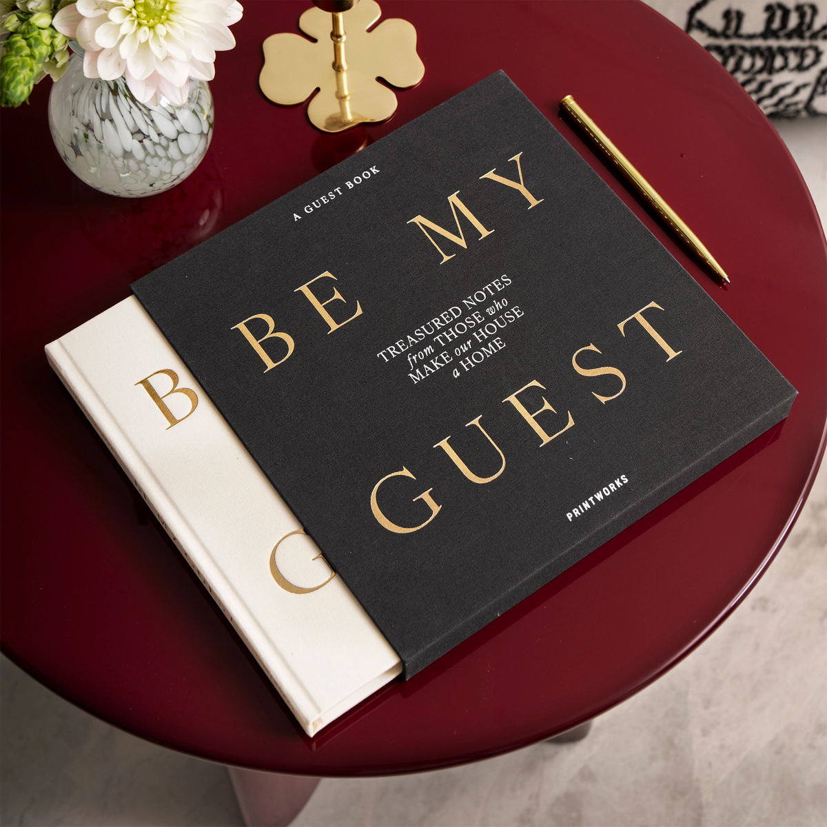 White Be My Guest guest book half out of its charcoal sleeve on a round red table