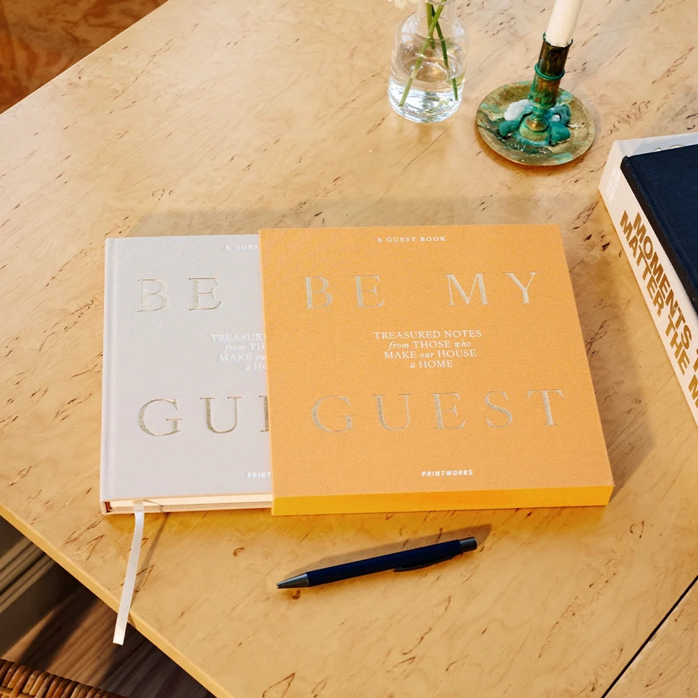 Beige Be My Guest guest book half out of its yellow sleeve on a beige marble table