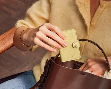 Vrouw stopt Secrid miniwallet geel in schoudertas.