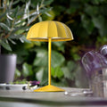 Sompex Ombrellino Oplaadbare Buitenlamp│Geel│art. 78353│op buitentafel met struiken op achtergrond