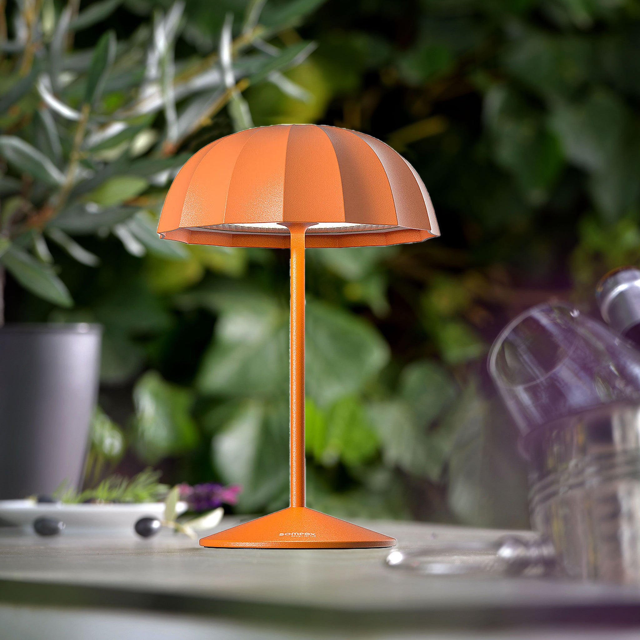 Sompex Ombrellino Oplaadbare Buitenlamp│Oranje│art. 78357│op buitentafel met struiken op achtergrond