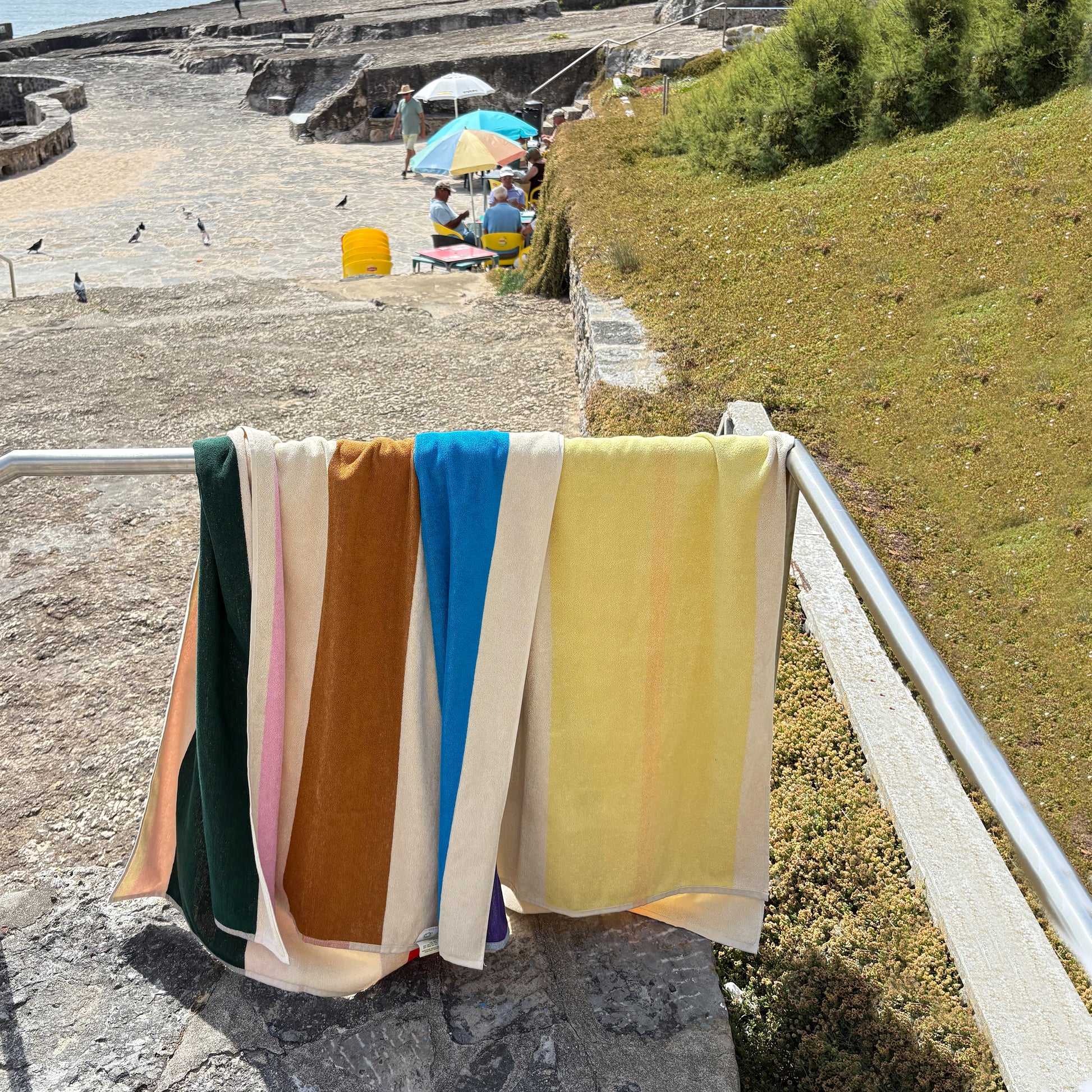 Strandlaken Martens & Martens Aqua Orange Purple & Yellow Suite702│art. CMMTT90AQORPUYE│2 soorten over railing aan strand