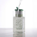 Dopper Travel Mug Small 300ml Forest Green - met glas op voorgrond waarin water met koolzuur wordt geschonken