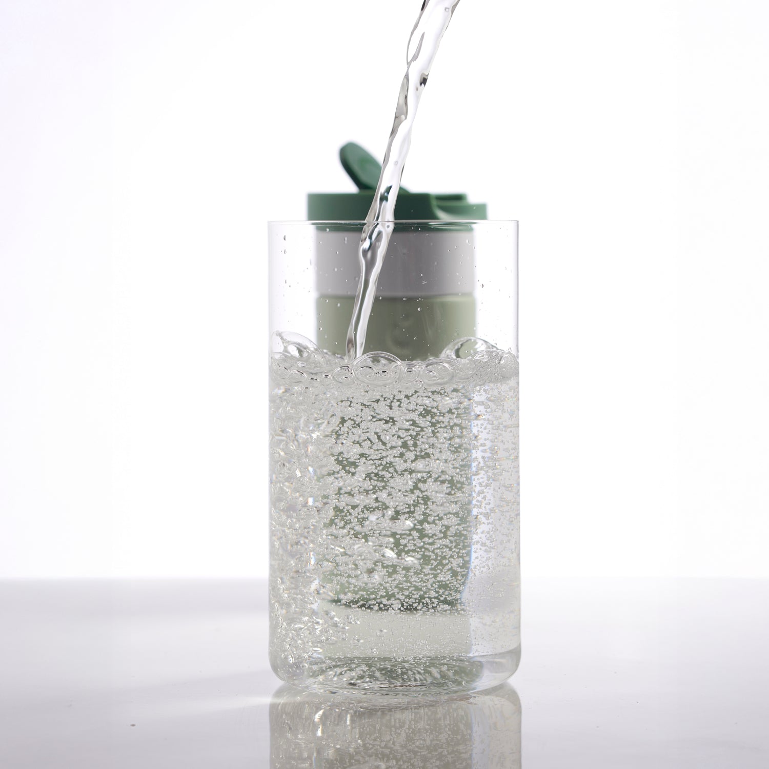 Dopper Travel Mug Small 300ml Forest Green - met glas op voorgrond waarin water met koolzuur wordt geschonken