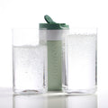 Dopper Travel Mug Small 300ml Forest Green - vooraanzicht met twee glazen op voorgrond met koolzuurhouden water