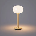 ELLE Decoration Vendome table lamp in matt gold with the light on, against a grey background.