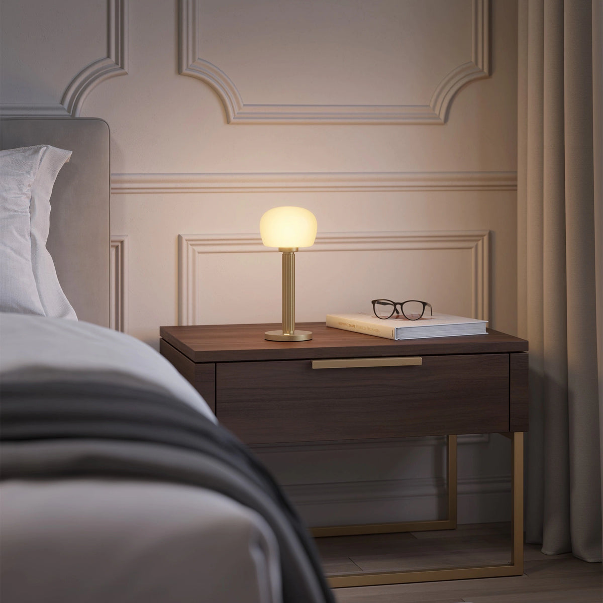 ELLE Decoration Vendome table lamp in matt gold on a bedside table next to a bed.