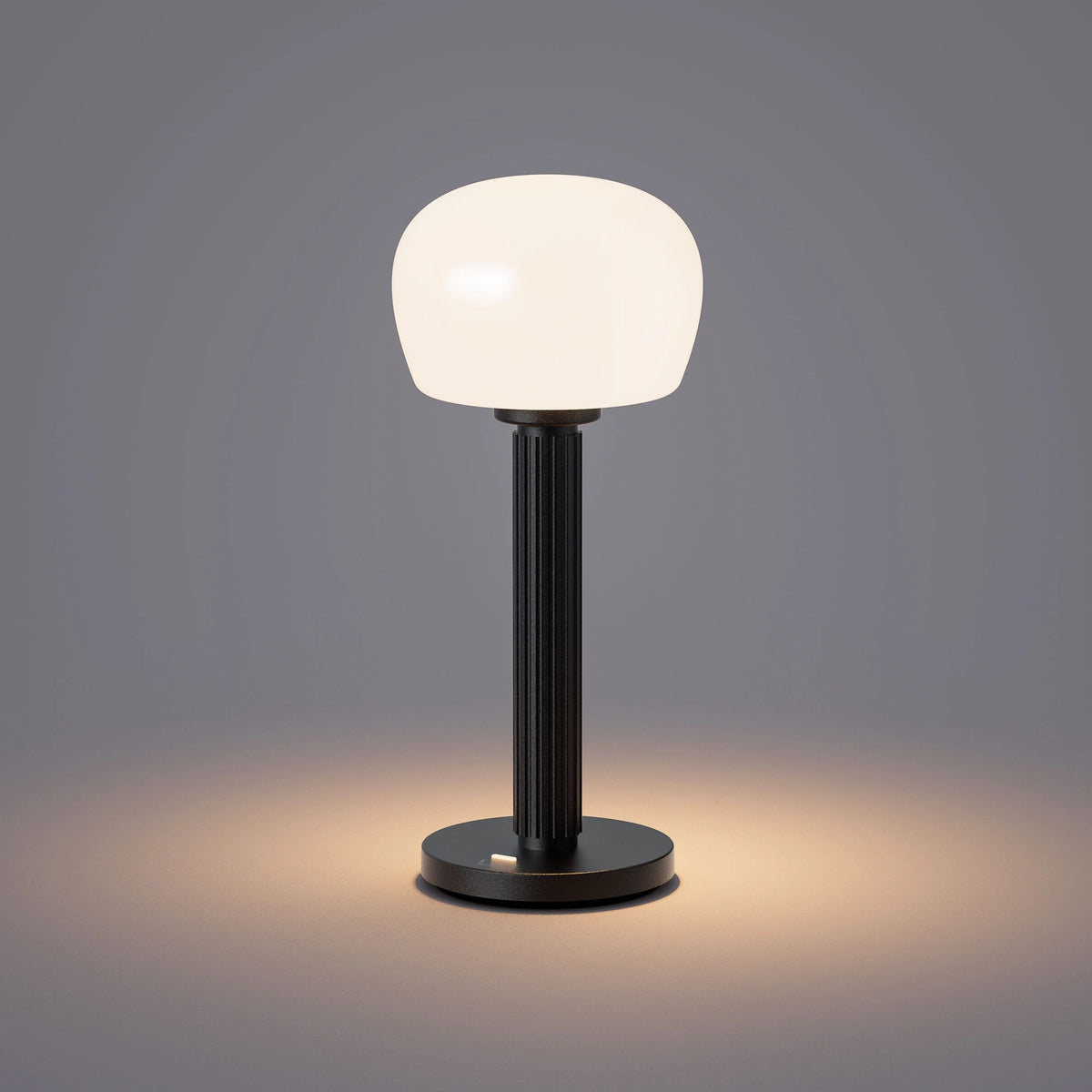 ELLE Decoration Vendome table lamp in matt black with the light on, against a grey background.
