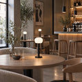 Several ELLE Decoration Vendome table lamps in matt black on tables in a restaurant.