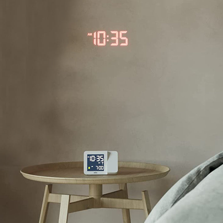 Braun Projectieklok en Wekker Digitaal BC15W-DCF│Wit│Radiogestuurd│op houten tafeltje met tijd op muur geprojecteerd