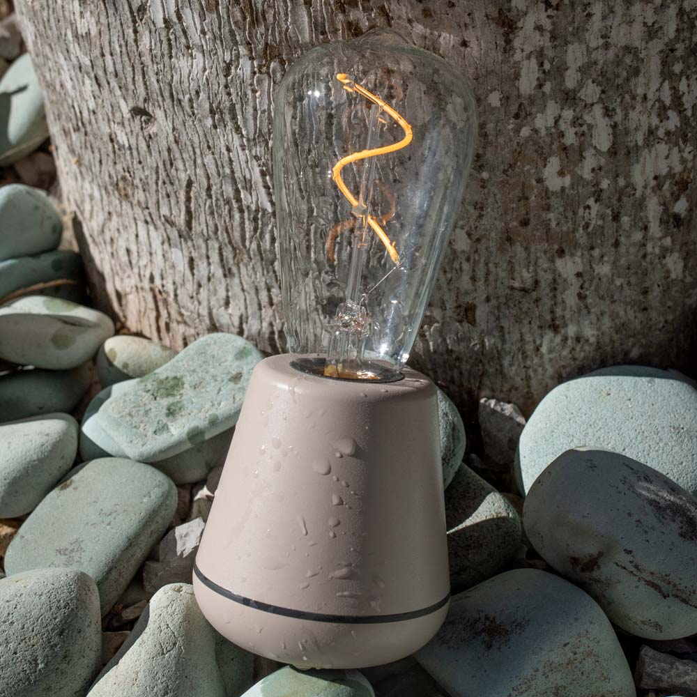 Humble One Outdoor Oplaadbare Tafellamp Linen│Buitenverlichting│art. UMTL00119│op losse stenen met waterdruppels en licht aan