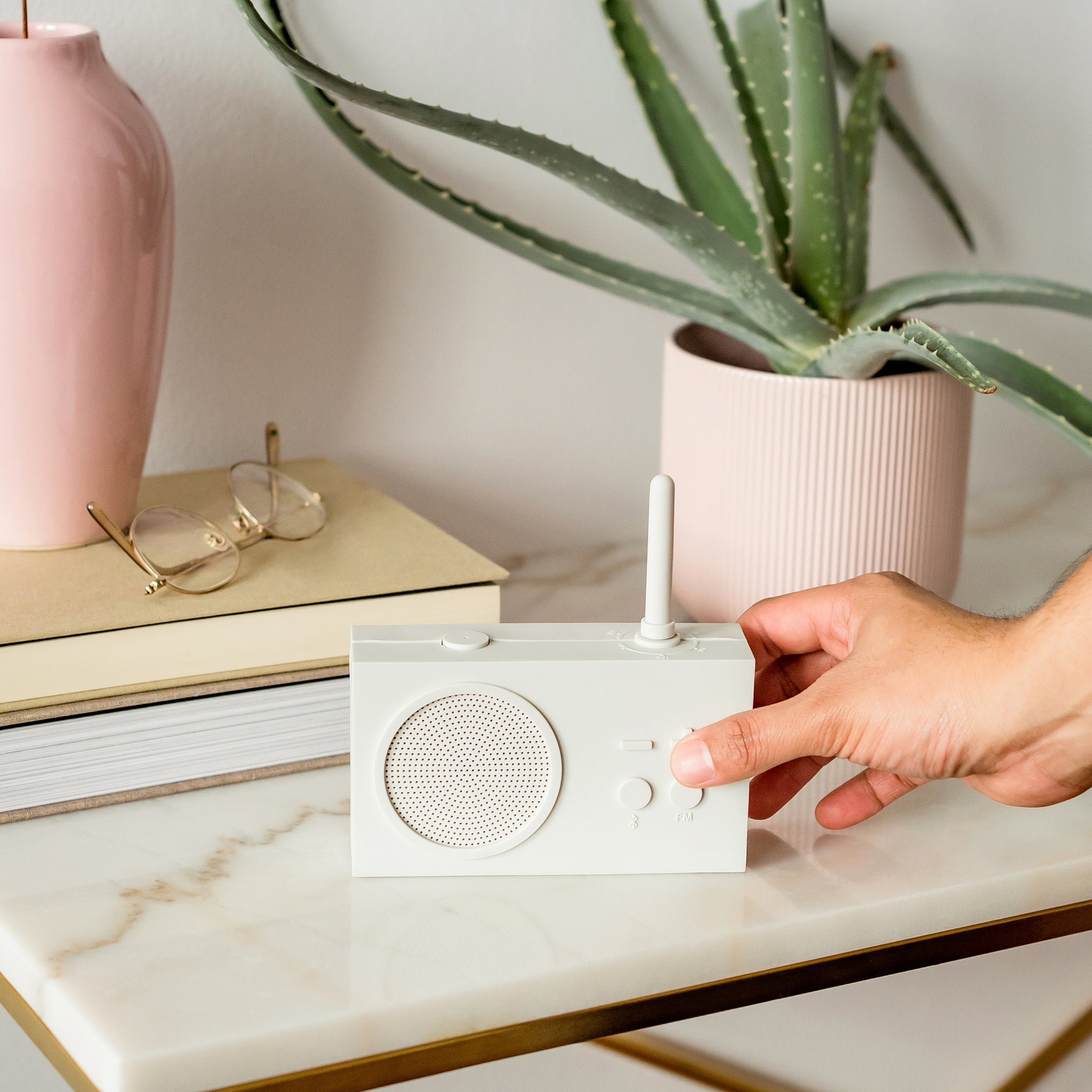 Lexon Tykho-3 FM Radio en Bluetooth-speaker│Lichtgrijs│oplaadbaar│art. LA119W7│op marmeren tafel met hand op toets