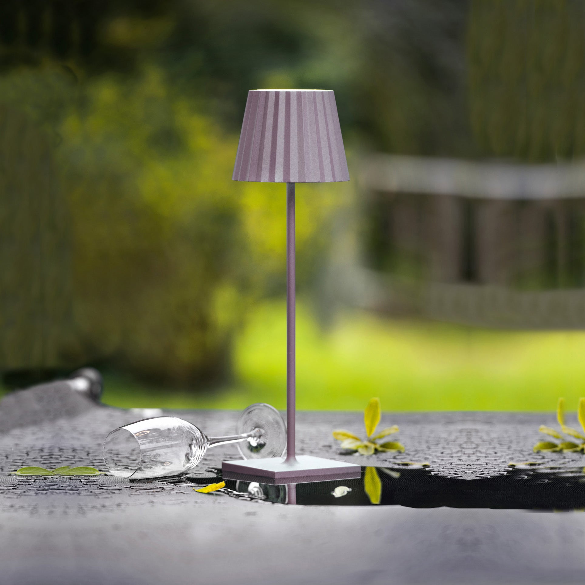 Sompex Troll 2.0 Roze│Oplaadbare tafellamp│Buitenverlichting│art. 78177│op buitentafel met regendruppes en leeg wijnglas