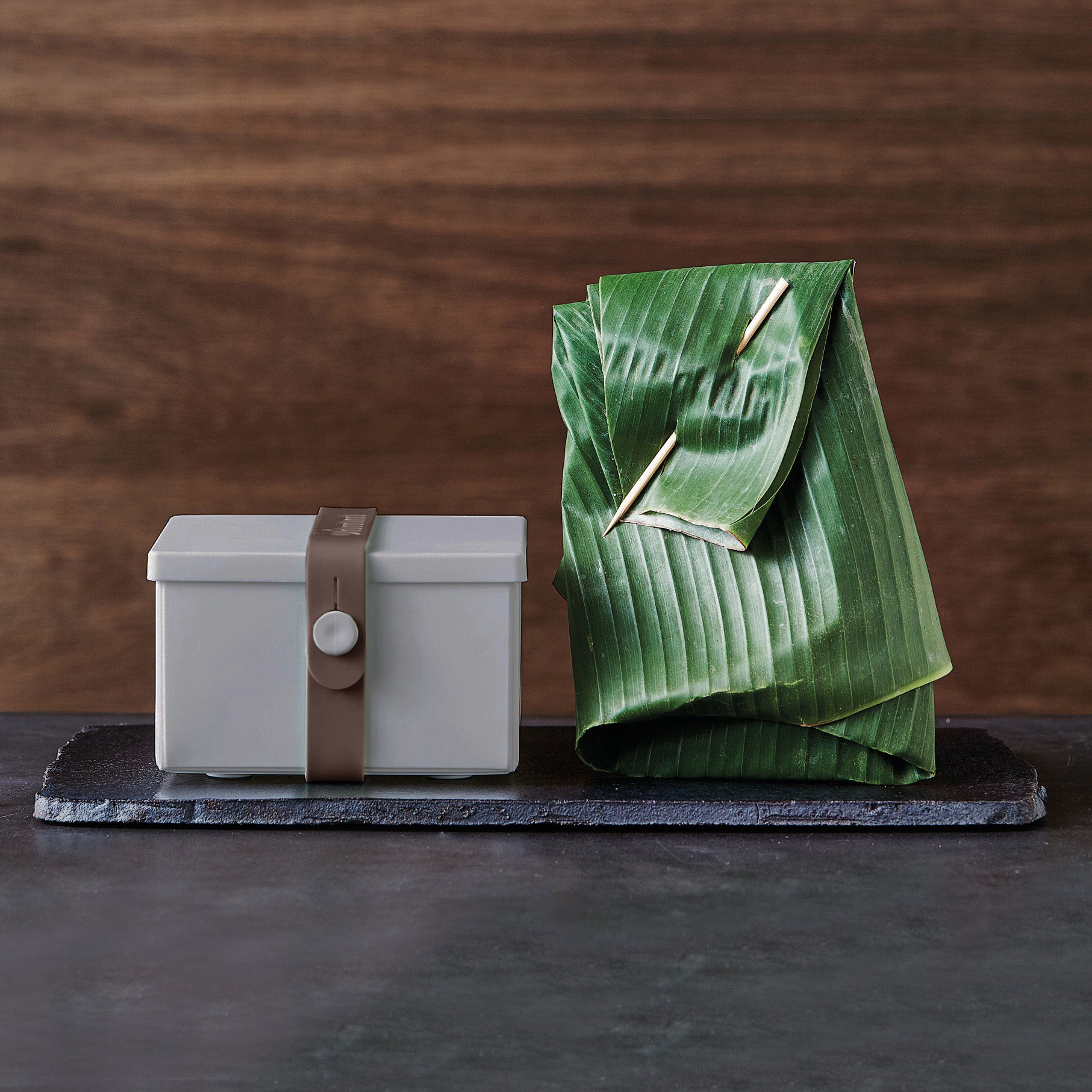 Uhmm 02 Opvouwbare Lunchbox Lightgrijs│art. 982411│met strap bruin naast zakje van bladeren